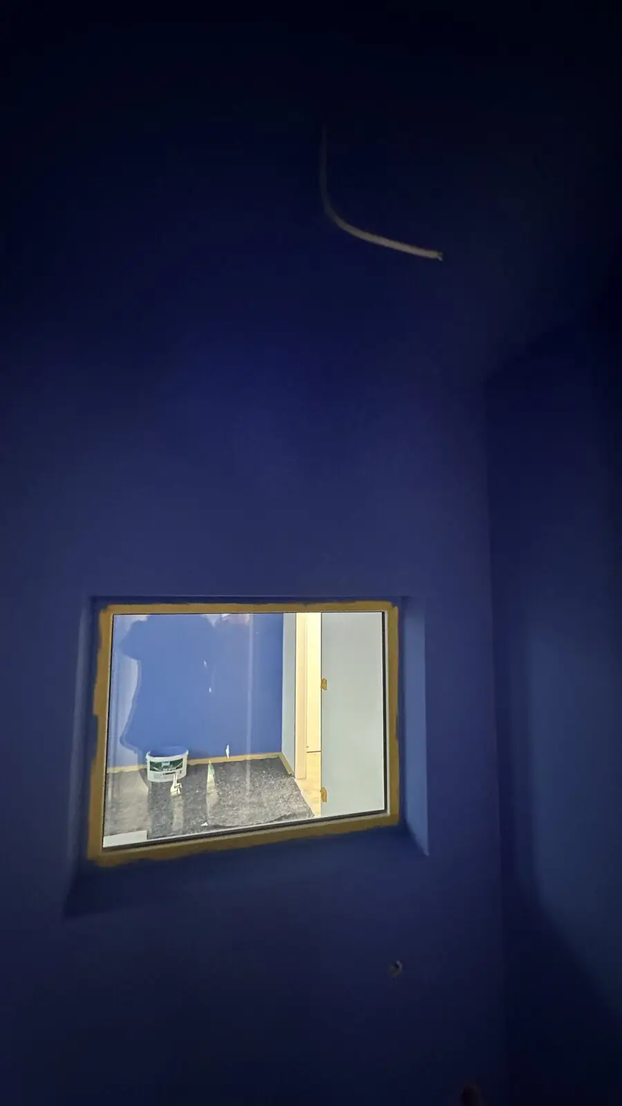 Window opening in a blue wall, a cable hanging above it