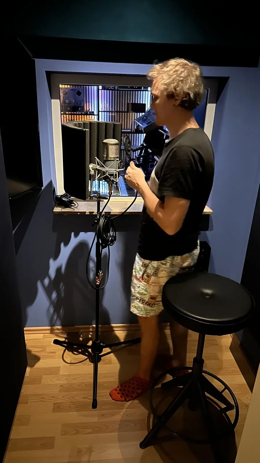 A singer at the microphone in the booth, the window to the control room behind