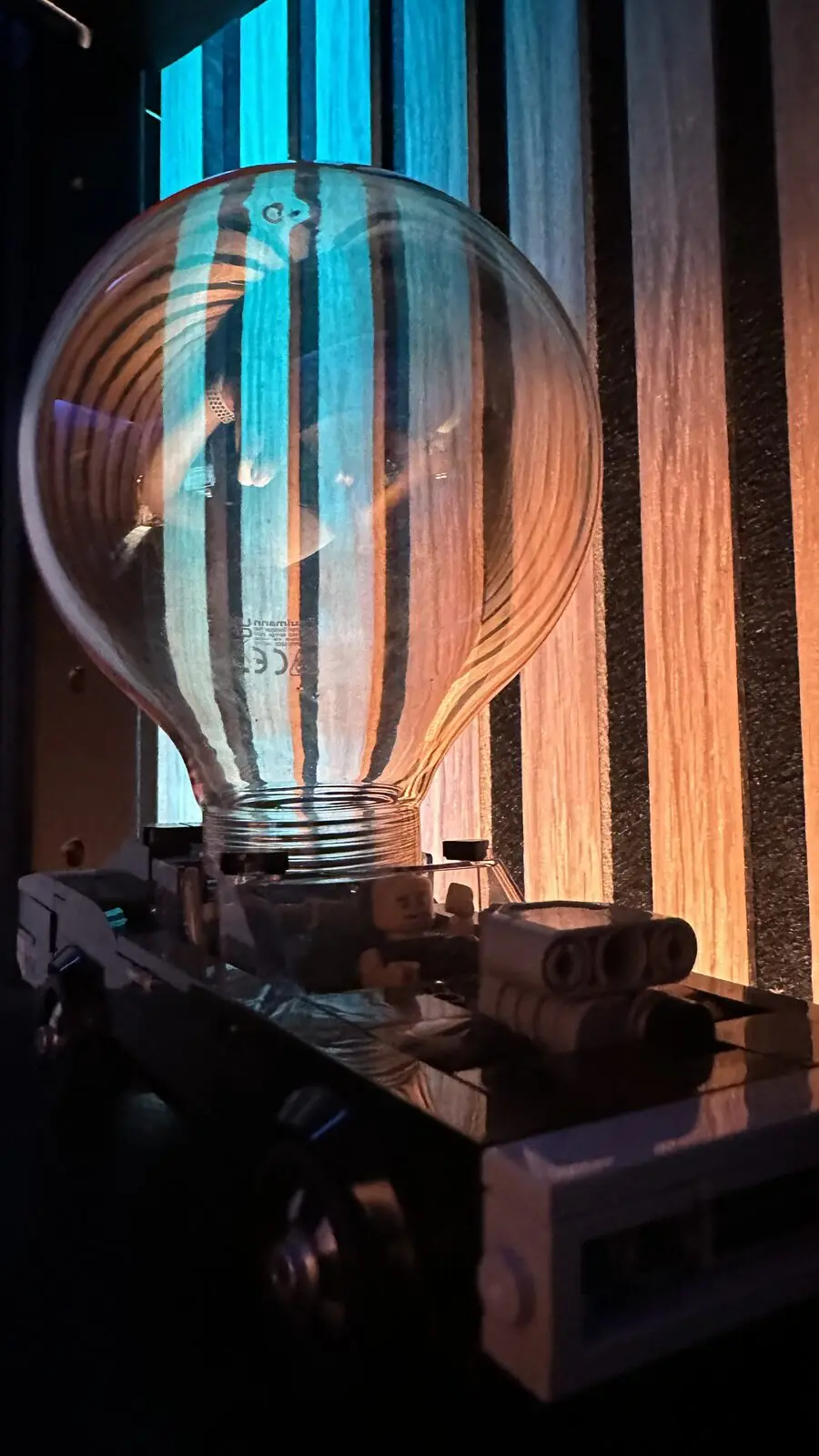 A large bulb in front of the lit slatted wall