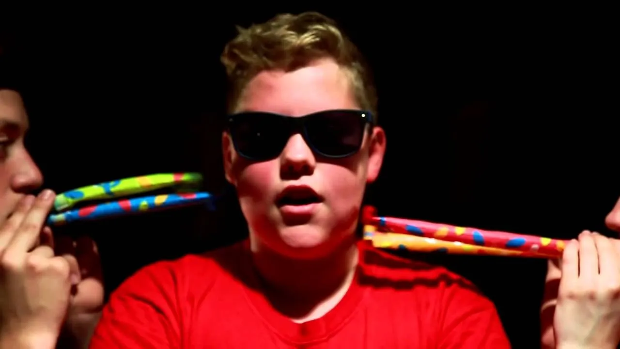 Still from the KDS Crew music video: a young rapper in sunglasses and a red shirt facing the camera