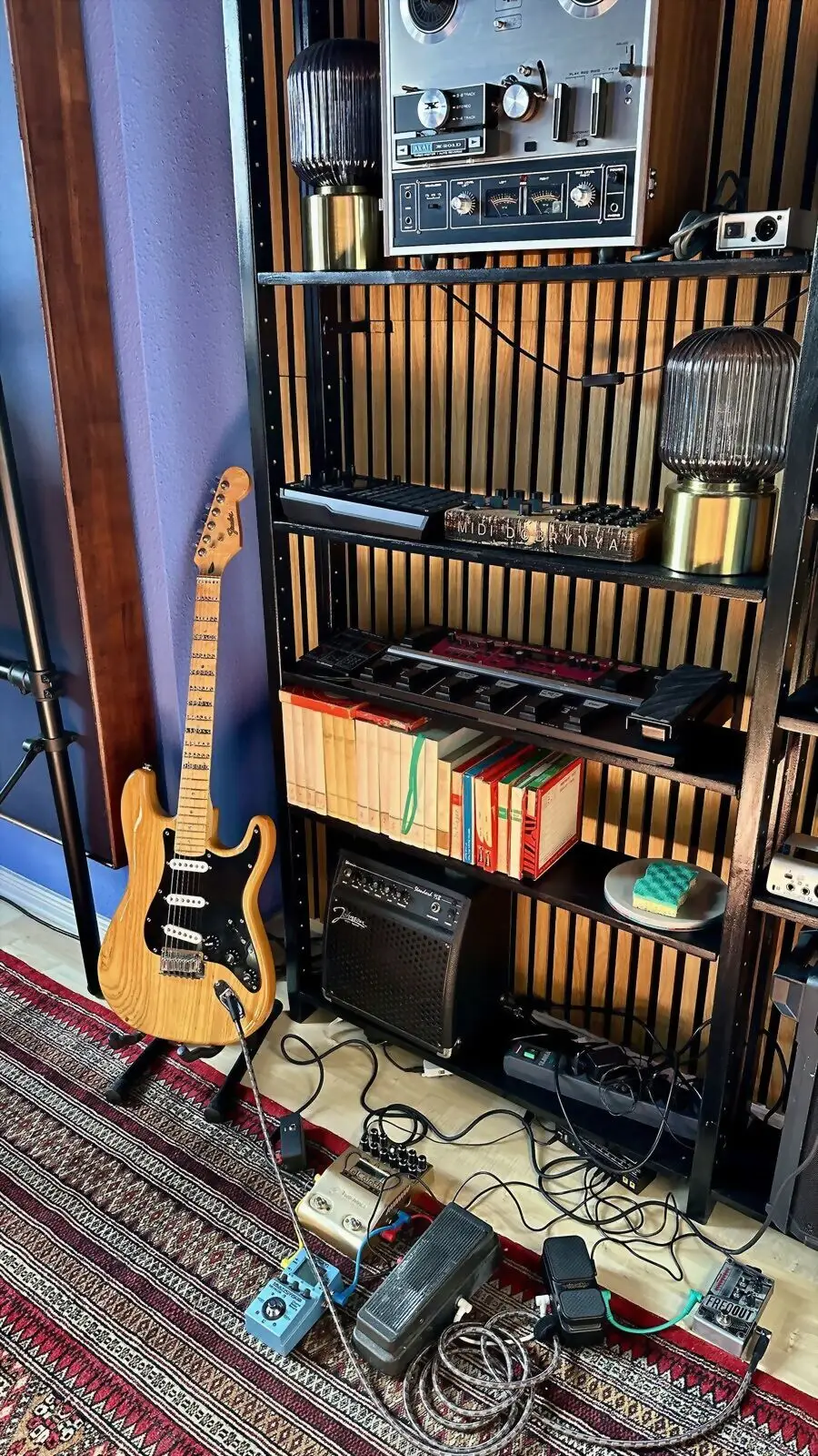 Electric guitar and pedals in front of the slatted wall
